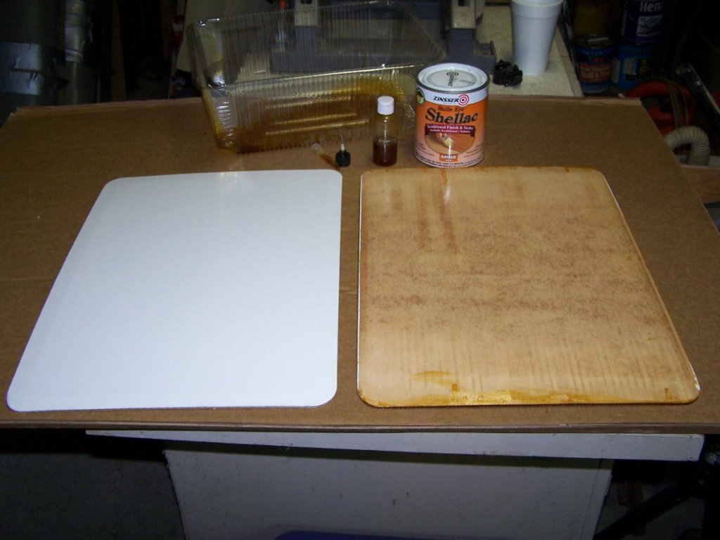 The panel on the left is actually a precut cake board, straight out of the box, gloss finish on one side, corners already cut in a radius. The one on the right has the inside shellacked. Note the shellac and tools above.
