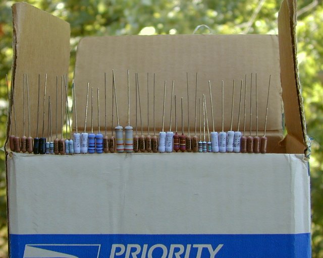 Resistors - In Order - On edge of box - Here is an old trick from the Heathkit and Dynaco kit building days. Line up your parts in order and slip the leads into the edge of a cardboard box like this. You won't be chasing them around on the table and you'll minimize errors when "stuffing" your Printed Circuit board. But be VERY careful with the tiny little metal film resistors. They can EASILY slide down into the side of the box. Just be careful, and you *should* be fine.